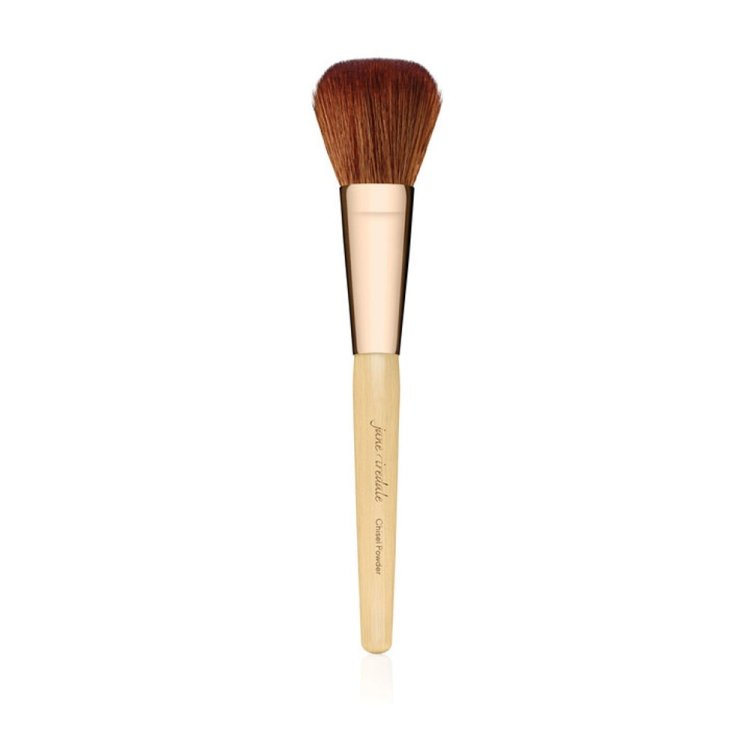 Na zdjęciu jest pędzel Jane Iredale Chisel Powder Brush. Włosie  miękkie, gęste, naturalnie ułożone w zaokrąglony kształt, idealne do równomiernego rozprowadzania pudru.  Trzonek drewniany, w jasnym kolorze, z nazwą marki i oznaczeniem „Chisel Powder”.
