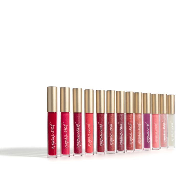 Na obrázku je vidět celá řada lesků Jane Iredale HydroPure Hyaluronic Lip Gloss. Každý má jedinečnou barvu a finiš – od transparentních, přes jemné růžové a broskvové odstíny až po výrazné červené a burgundské.
