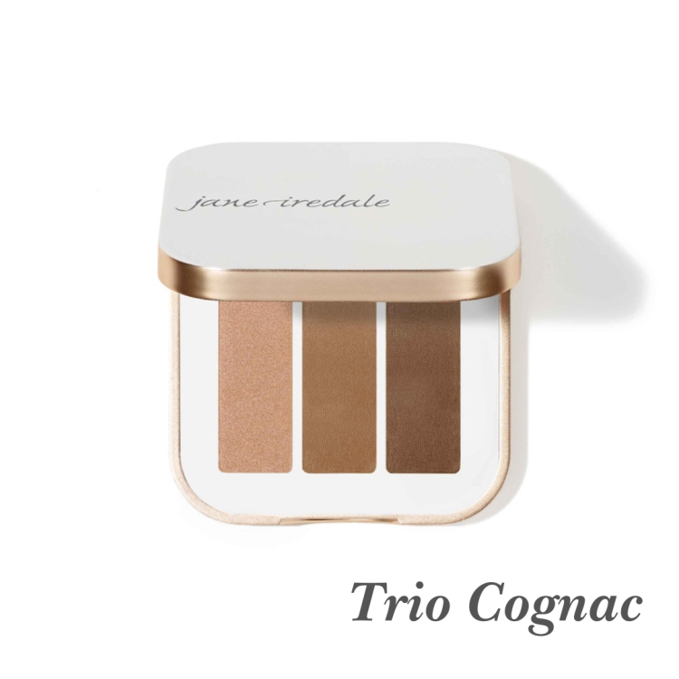 Na fotografii je trojitá paletka očních stínů Jane Iredale v odstínu Trio Cognac. Sada obsahuje tři odstíny v teplé hnědé tónině: třpytivá měděná hnědá, matná karamelová hnědá, matná kaštanová hnědá.