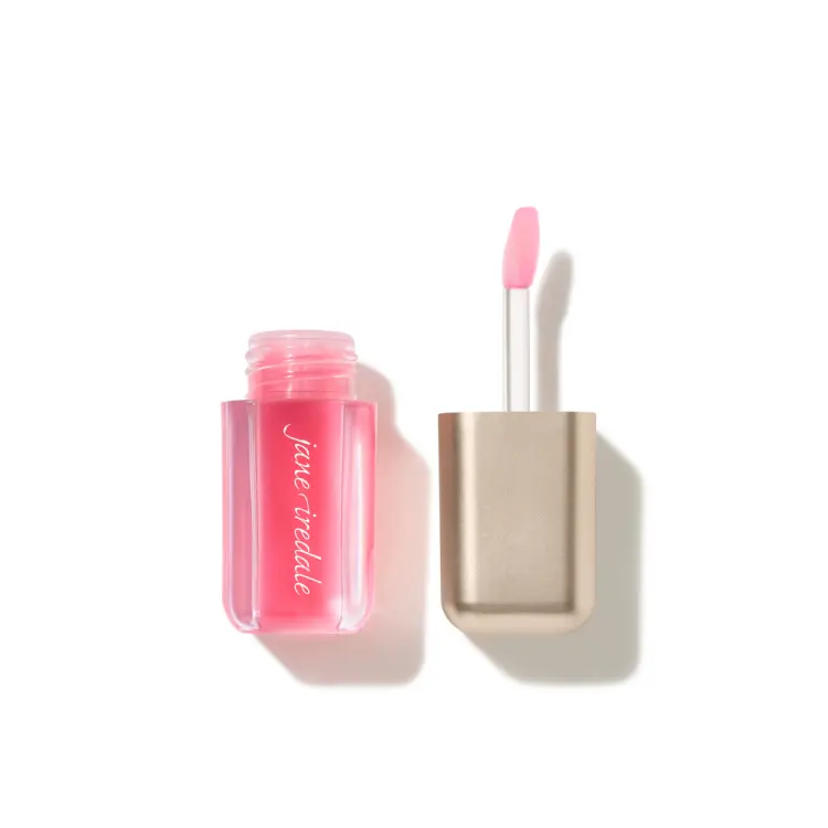Na bílém pozadí je otevřený olej na rty Jane Iredale Just Kissed Lip Oil v průhledném obalu v intenzivním růžovém odstínu. Vedle se nachází zlatý uzávěr s vysunutým aplikátorem s měkkou, zaoblenou špičkou pokrytou růžovým olejem.