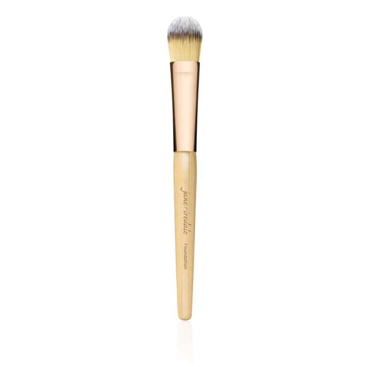 Na obrázku je štětec na make-up značky Jane Iredale. Má elegantní design – dřevěnou rukojeť v přírodní barvě se zlatou objímkou a husté, měkké štětiny v odstínech žluté a bílé.